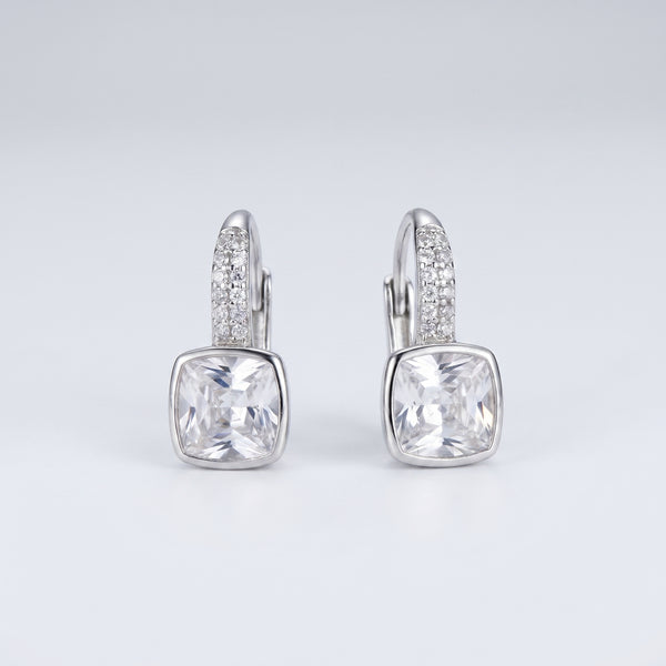 A pair of silver leverback earrings featuring a large cushion-cut clear gemstone in a bezel setting, with a pavé band of small clear stones above it, shown on a light gray gradient background.