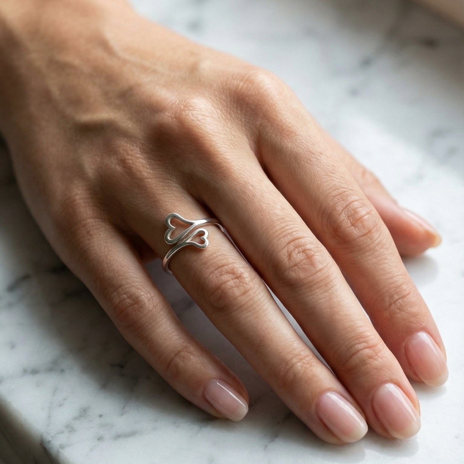 Hand wearing a silver ring on a marble surface