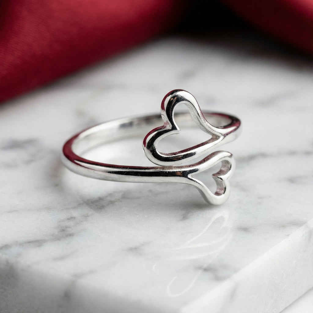 Silver ring with heart and bone design on a marble surface with red fabric in the background