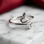 Silver ring with heart and bone design on a marble surface with red fabric in the background