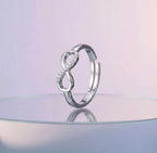 Silver infinity ring on a reflective surface with a pastel pink background
