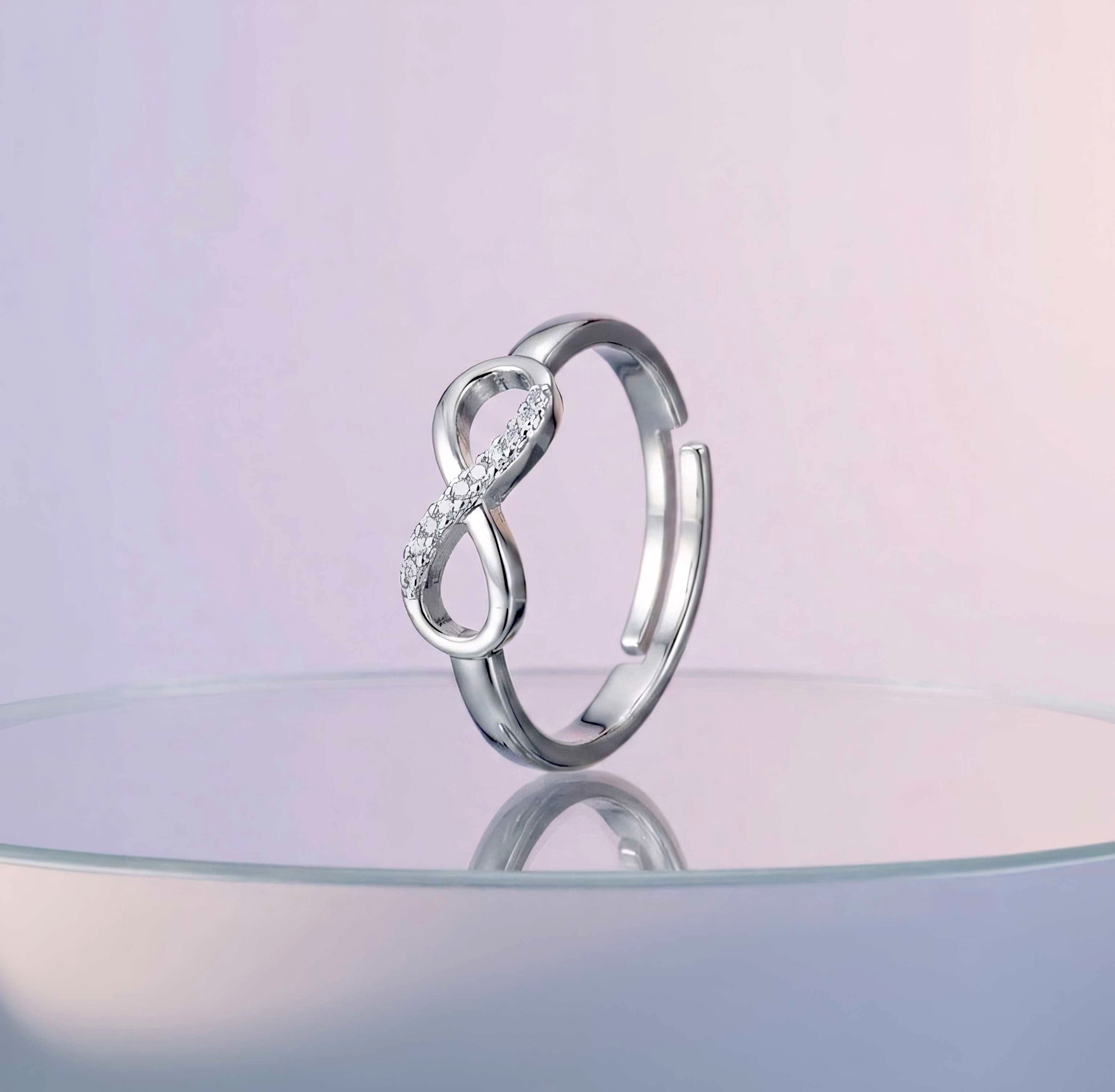 Silver infinity ring on a reflective surface with a pastel pink background