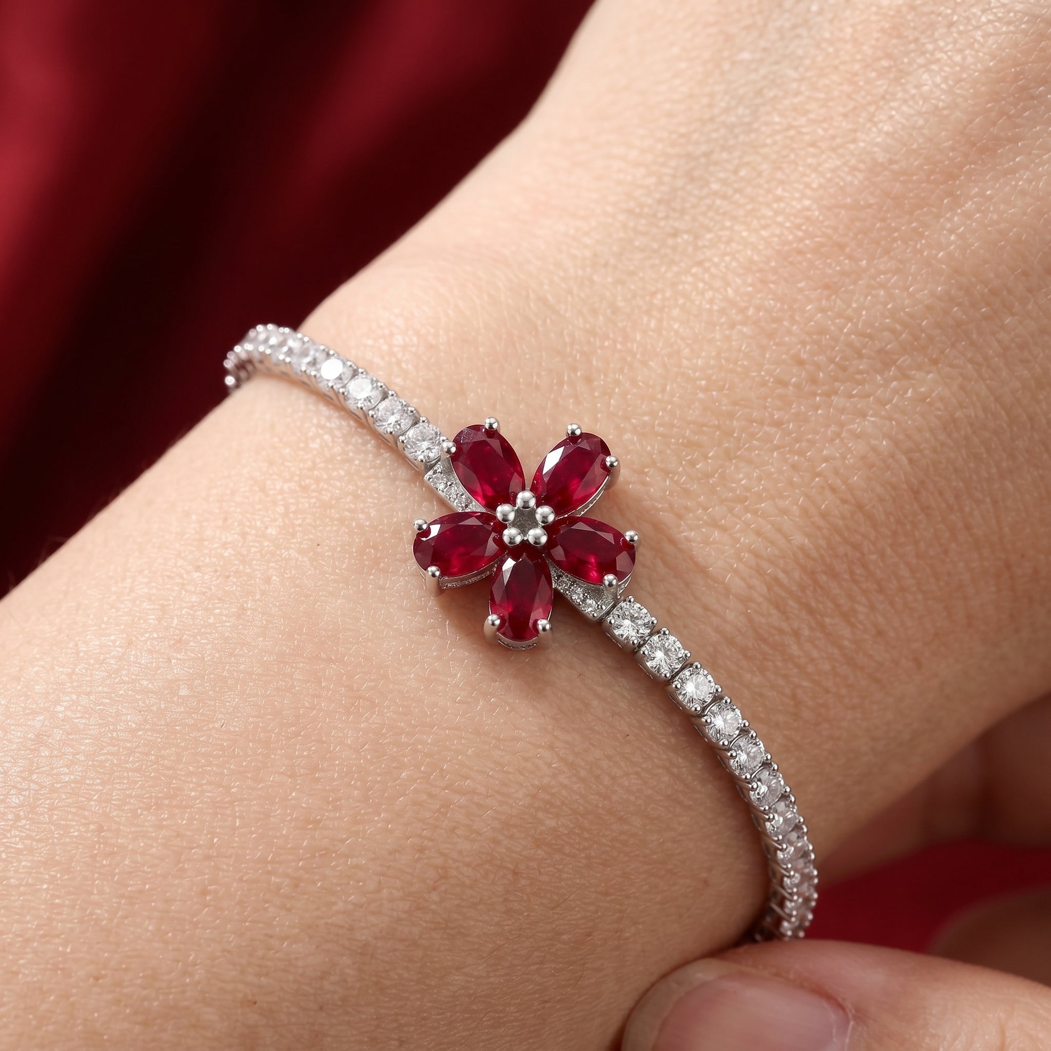 Bracelet with a red gemstone flower design on a wrist against a red background