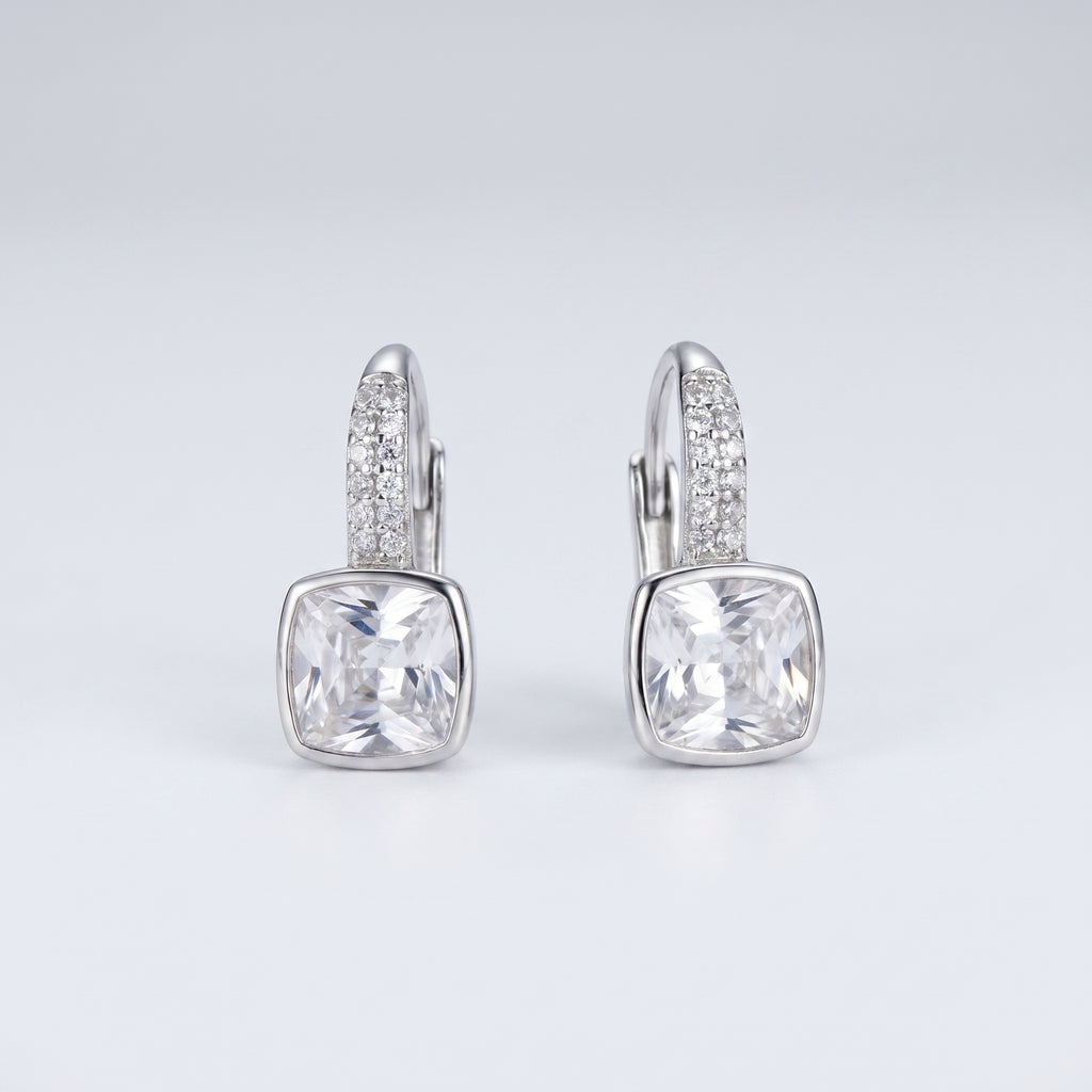 A pair of silver leverback earrings featuring a large cushion-cut clear gemstone in a bezel setting, with a pavé band of small clear stones above it, shown on a light gray gradient background.