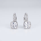 A pair of silver leverback earrings featuring a large cushion-cut clear gemstone in a bezel setting, with a pavé band of small clear stones above it, shown on a light gray gradient background.