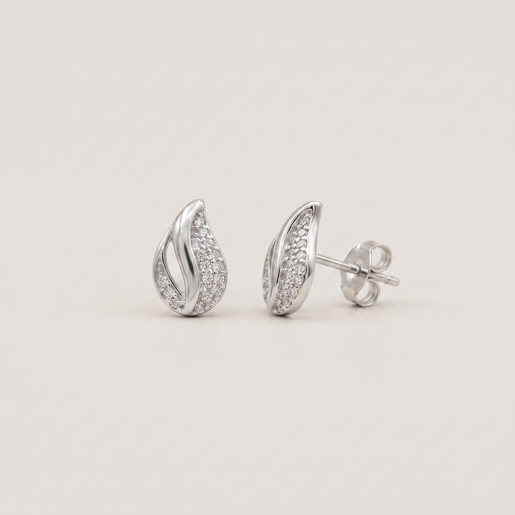 A pair of silver teardrop-shaped stud earrings paved with small clear stones, shown from both front and side angles on a light beige background.