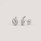 A pair of silver teardrop-shaped stud earrings paved with small clear stones, shown from both front and side angles on a light beige background.