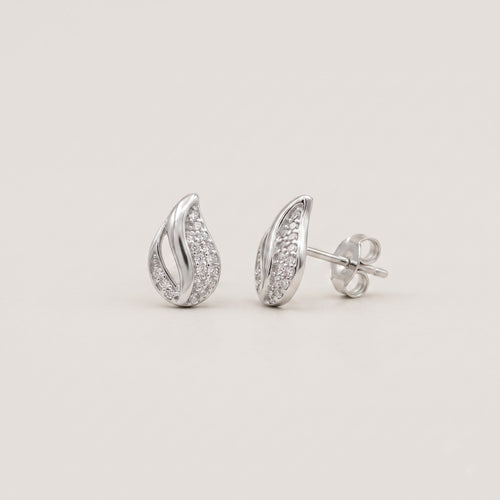 A pair of silver teardrop-shaped stud earrings paved with small clear stones, shown from both front and side angles on a light beige background.