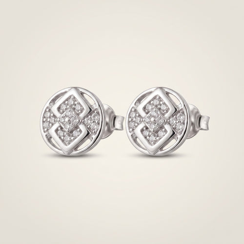 A pair of round silver stud earrings with a geometric interlocking pattern set with small clear pavé stones, shown on a light beige background.
