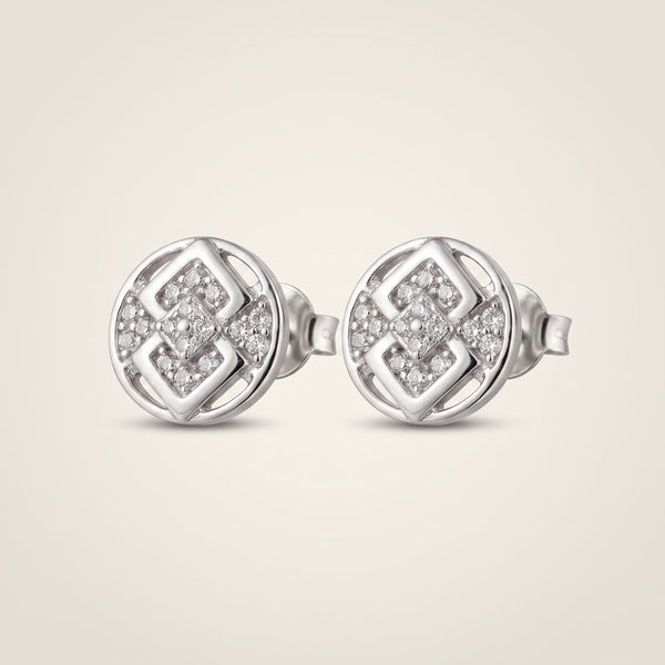 A pair of round silver stud earrings with a geometric interlocking pattern set with small clear pavé stones, shown on a light beige background.