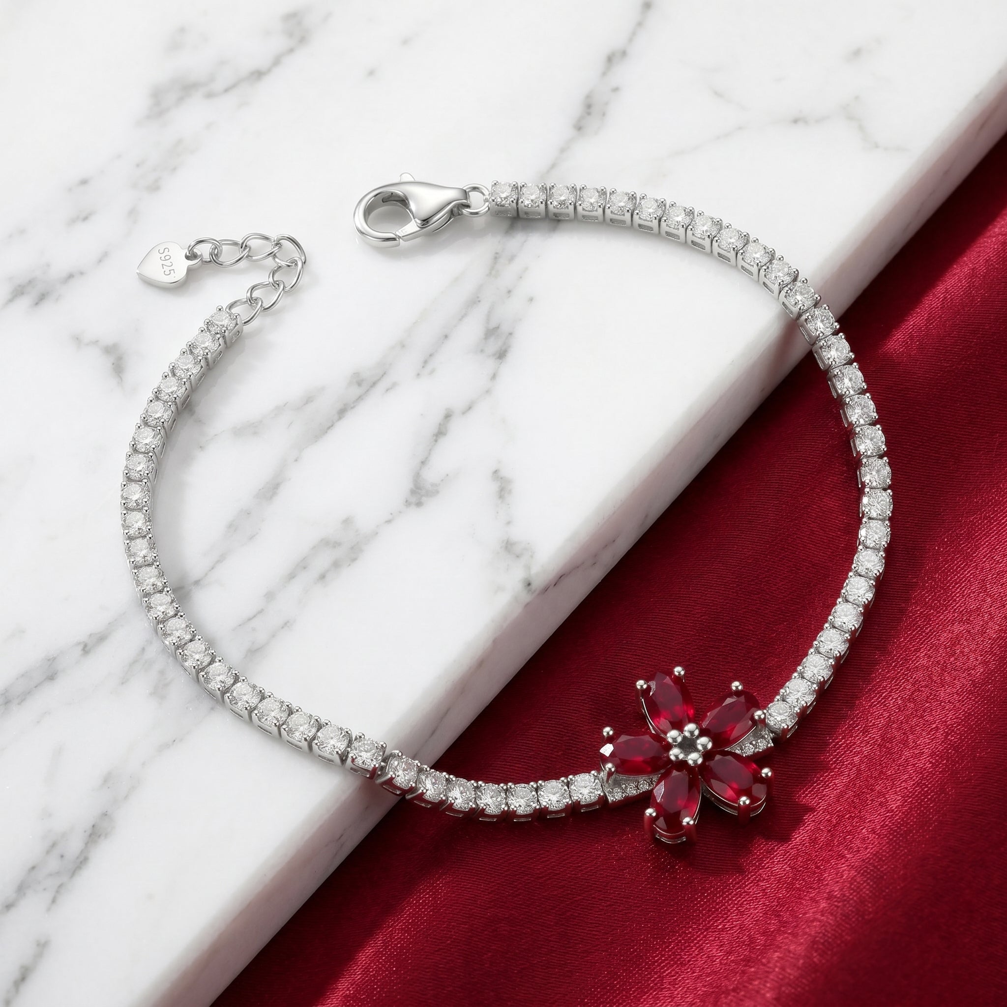 Silver bracelet with a red flower-shaped gemstone on a marble and red fabric background