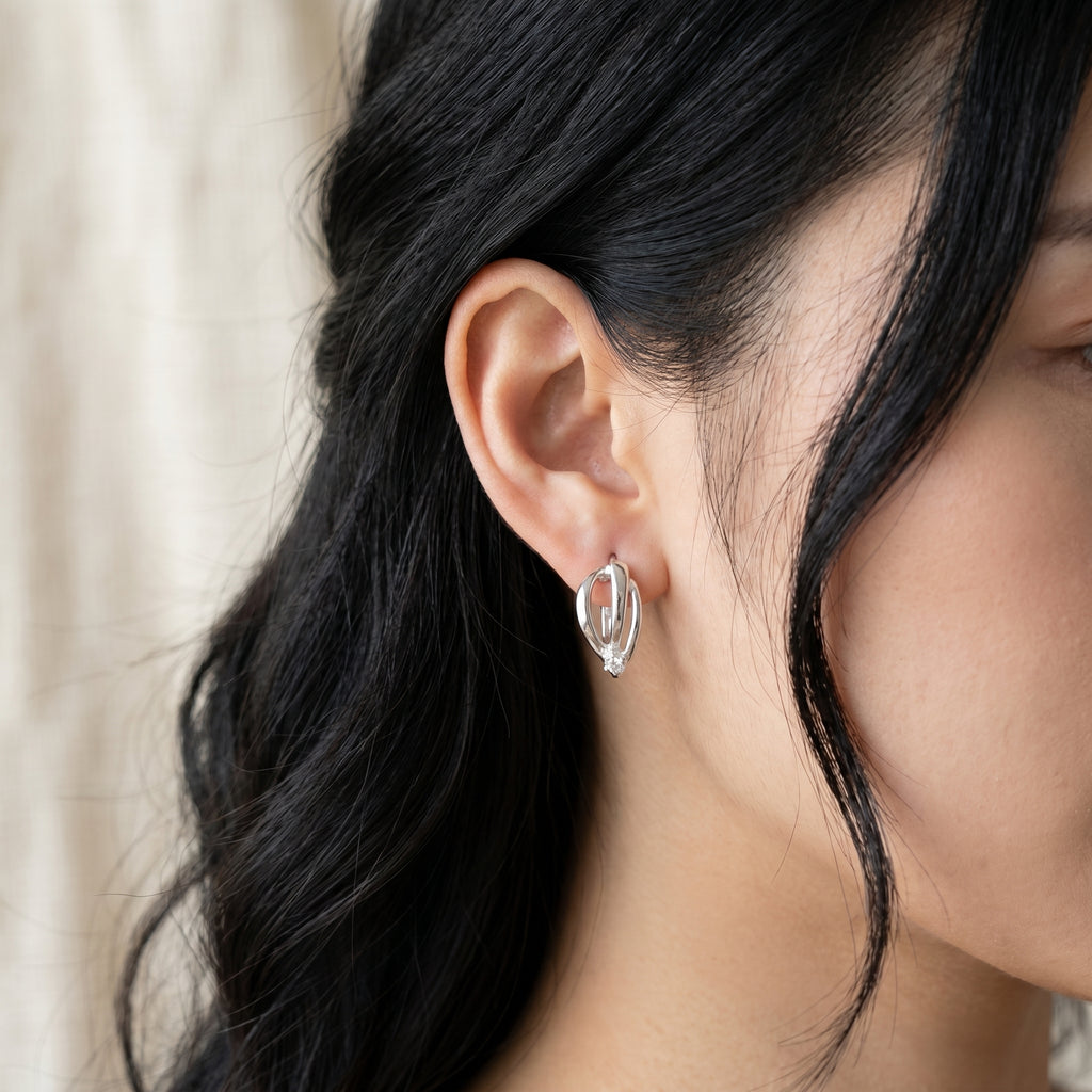 A close-up of a woman's ear wearing a small silver hoop earring with a polished, reflective finish.