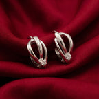 A pair of silver-toned huggie hoop earrings with a small clear crystal accent, displayed on draped red fabric.