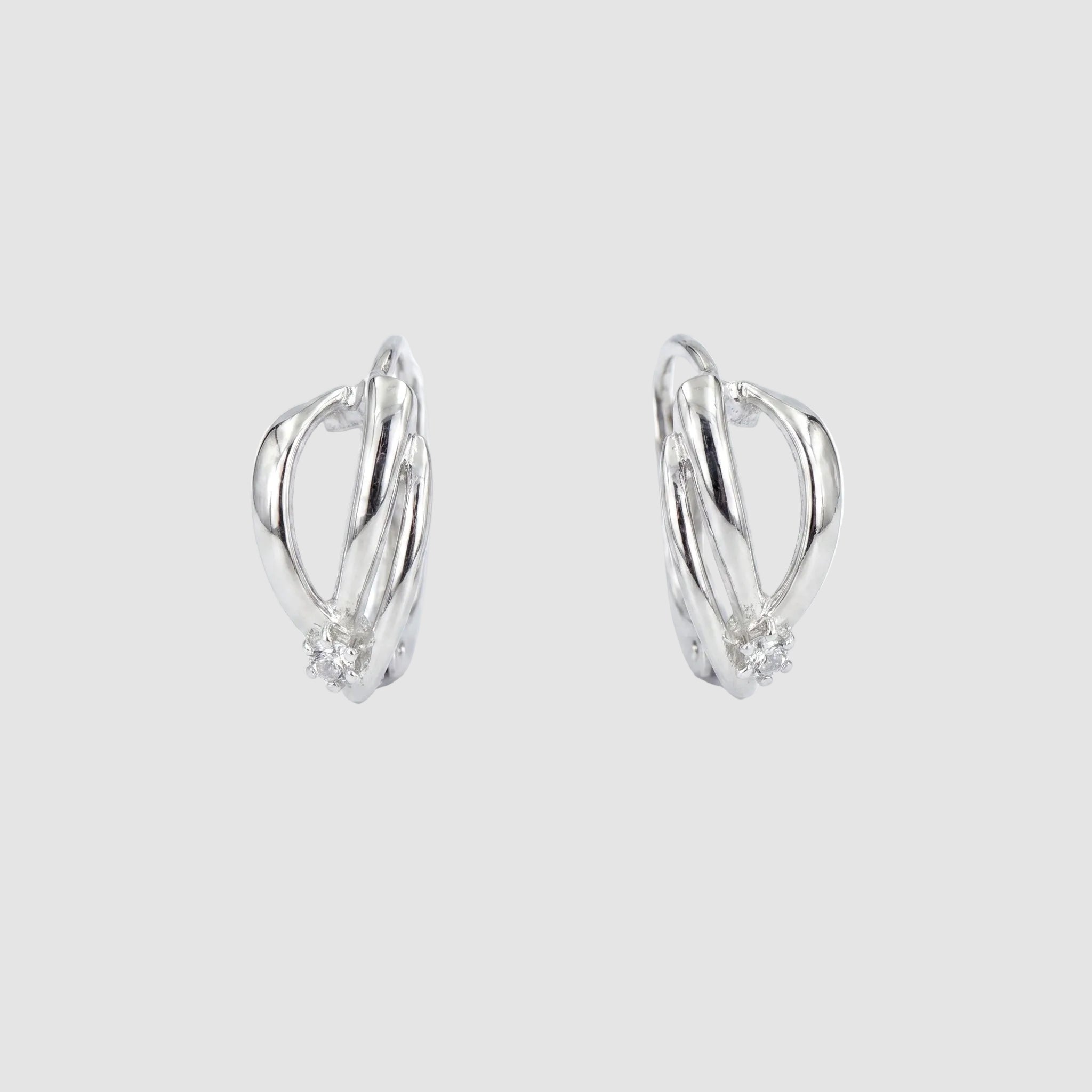 A pair of silver-toned huggie hoop earrings with a small cluster of clear stones at the bottom of each earring, shown on a plain white background.